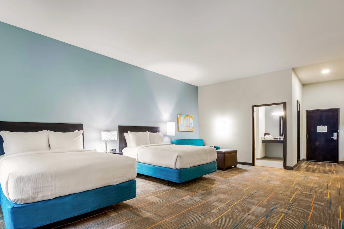 A hotel room with two beds, a nightstand, a lamp, and a painting on the wall.