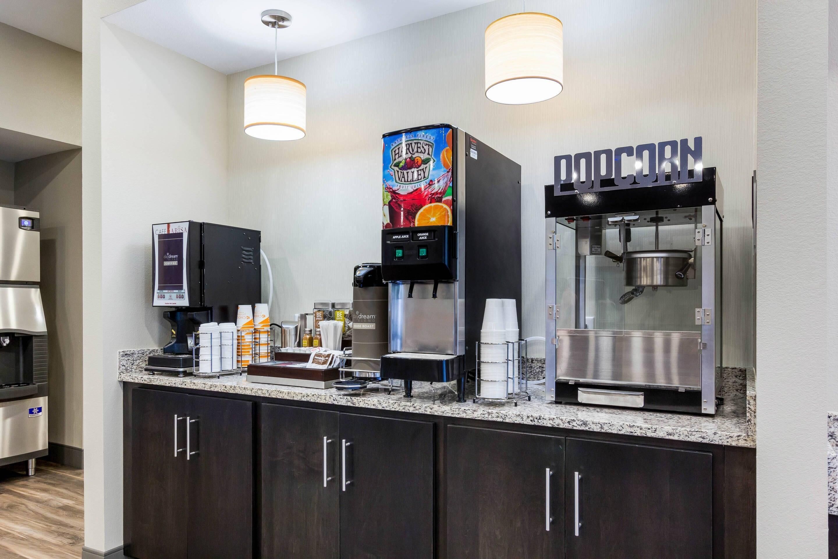 A self-service beverage station with a coffee machine, a juice dispenser, and a popcorn machine.