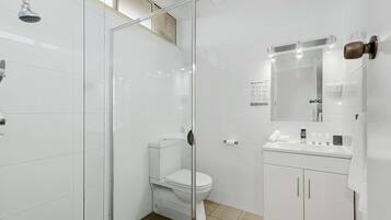 Een moderne badkamer met een glazen douchecabine, een wit toilet en een wastafelmeubel met spiegel en wastafel.