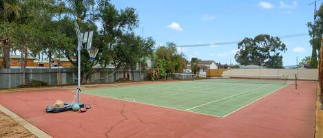 An outdoor tennis court with a net, surrounded by trees and a fence.