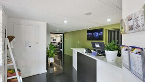 Un área de recepción con un escritorio blanco, una computadora, una planta en maceta y un televisor montado en la pared.