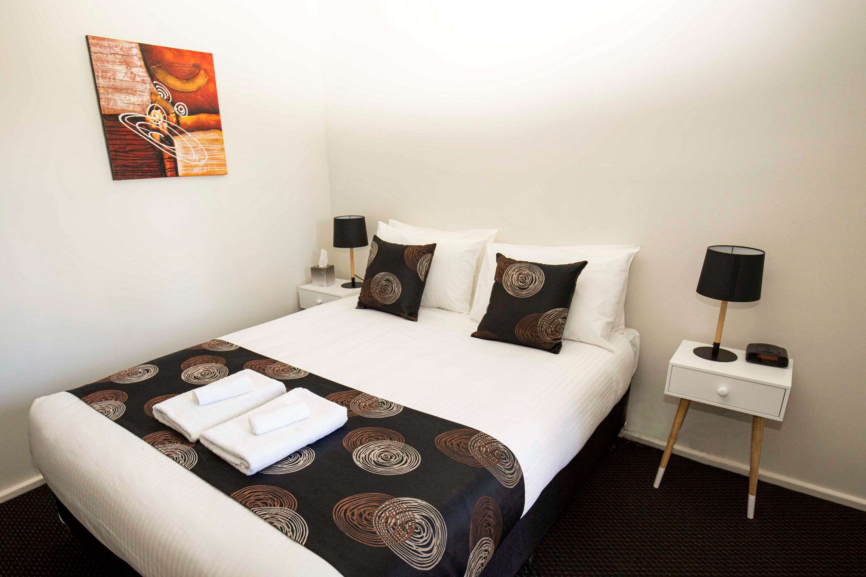 A neatly made bed with a black and brown patterned bedspread, white pillows, and two white towels folded at the foot of the bed.
