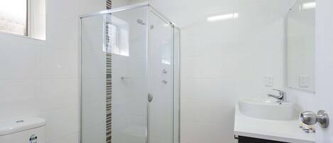Un baño con ducha envuelta en vidrio, un lavamanos blanco y un mueble de tocador oscuro.
