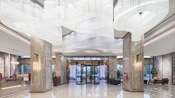 A spacious lobby with a revolving door, marble columns, and a modern chandelier. - Ramada by Wyndham Zhangjiajie (Zhangjiajie)