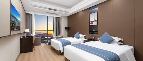 A hotel room with two beds, a desk, a chair, a TV, and a large window with a city view.