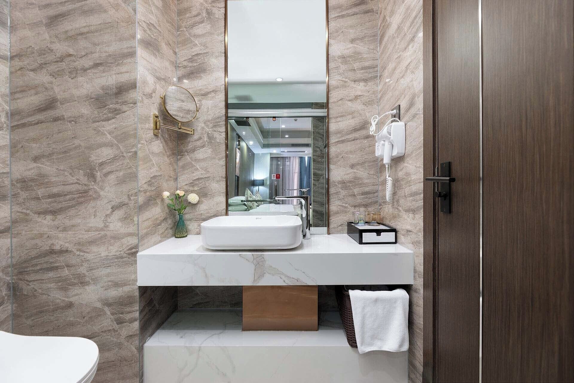 A bathroom with a marble wall, a white sink, a mirror, a telephone, and a towel rack.