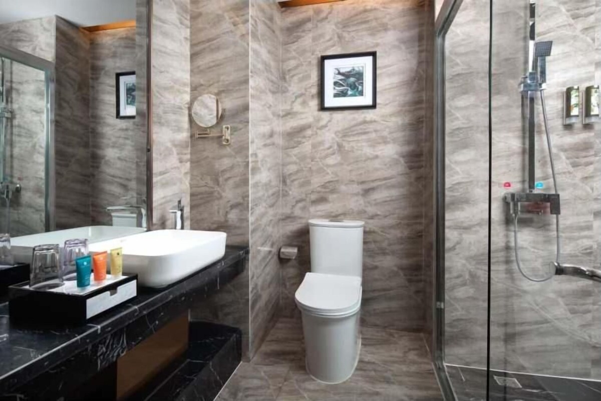 Une salle de bain avec un mur en marbre, un lavabo blanc, des toilettes et une douche.