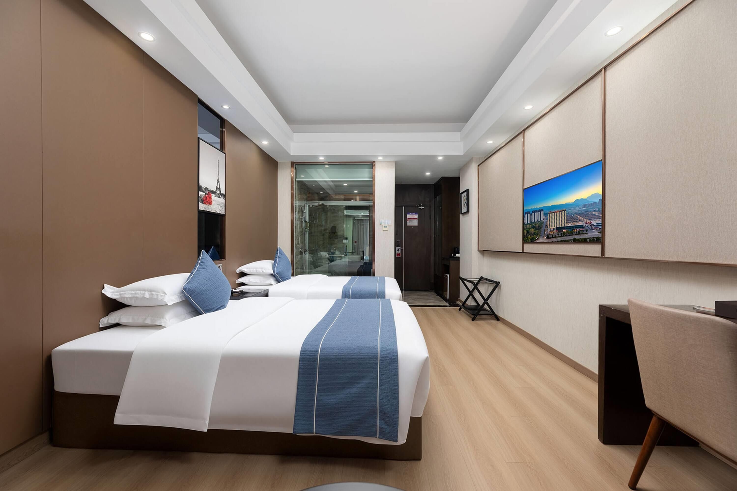 Hotelkamer met twee bedden, een bureau, een stoel, een schilderij aan de muur en uitzicht op de stad.