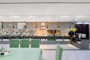 A modern restaurant with a long counter, green chairs, and a variety of dishes displayed. - Ramada by Wyndham Zhangjiajie (Zhangjiajie)
