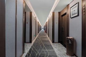 Ein Hotelgang mit mehreren Türen, einem gemusterten Teppich und einem Mülleimer.