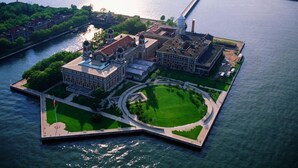 Una vista aerea di un ampio complesso di edifici storici con un cortile centrale, circondato da acqua e vegetazione.