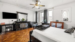 Una camera da letto con un letto grande, una ventola a soffitto, una TV a schermo piatto, una cassettiera in legno e una finestra con tende.