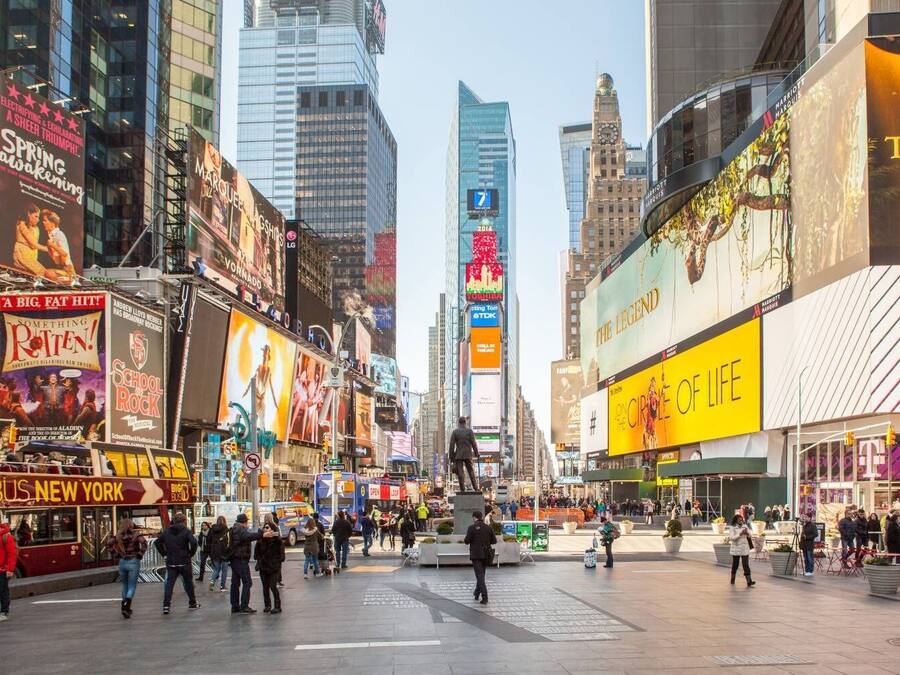 A busy urban square with large billboards and advertisements, surrounded by high-rise buildings.