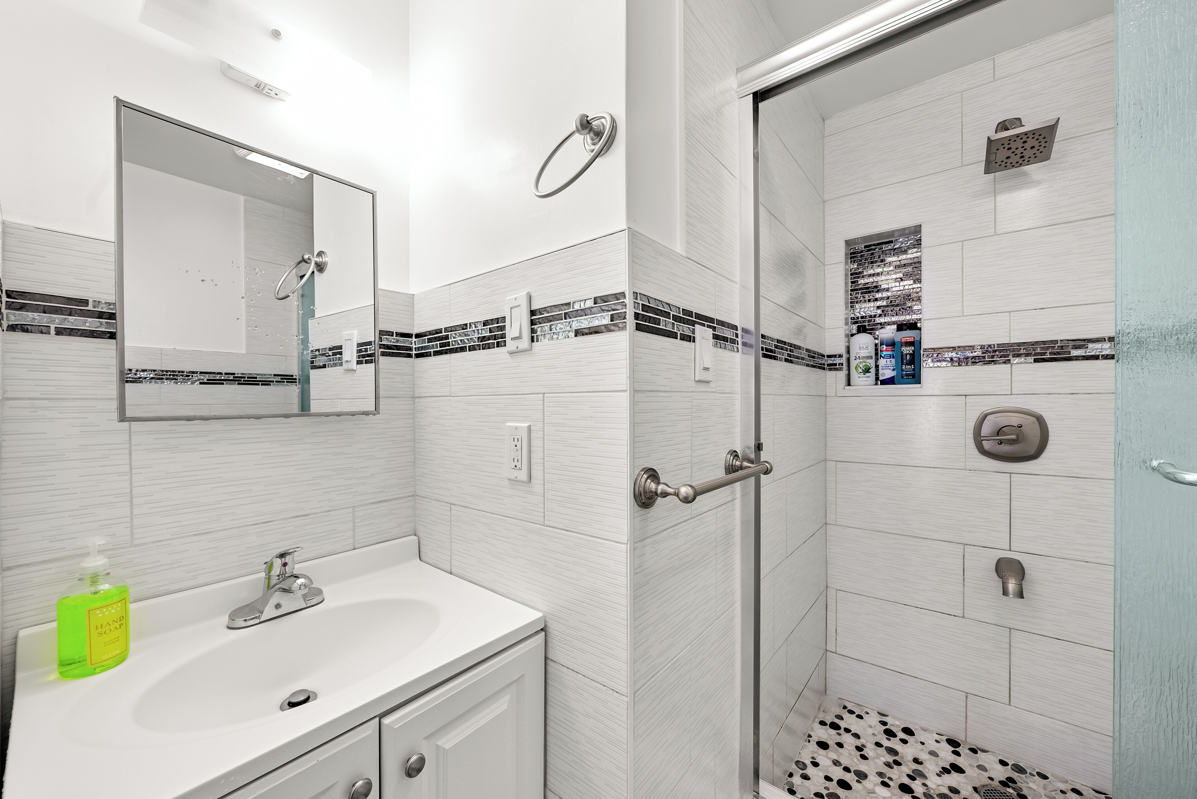 A modern bathroom with a white sink, mirror, and shower.