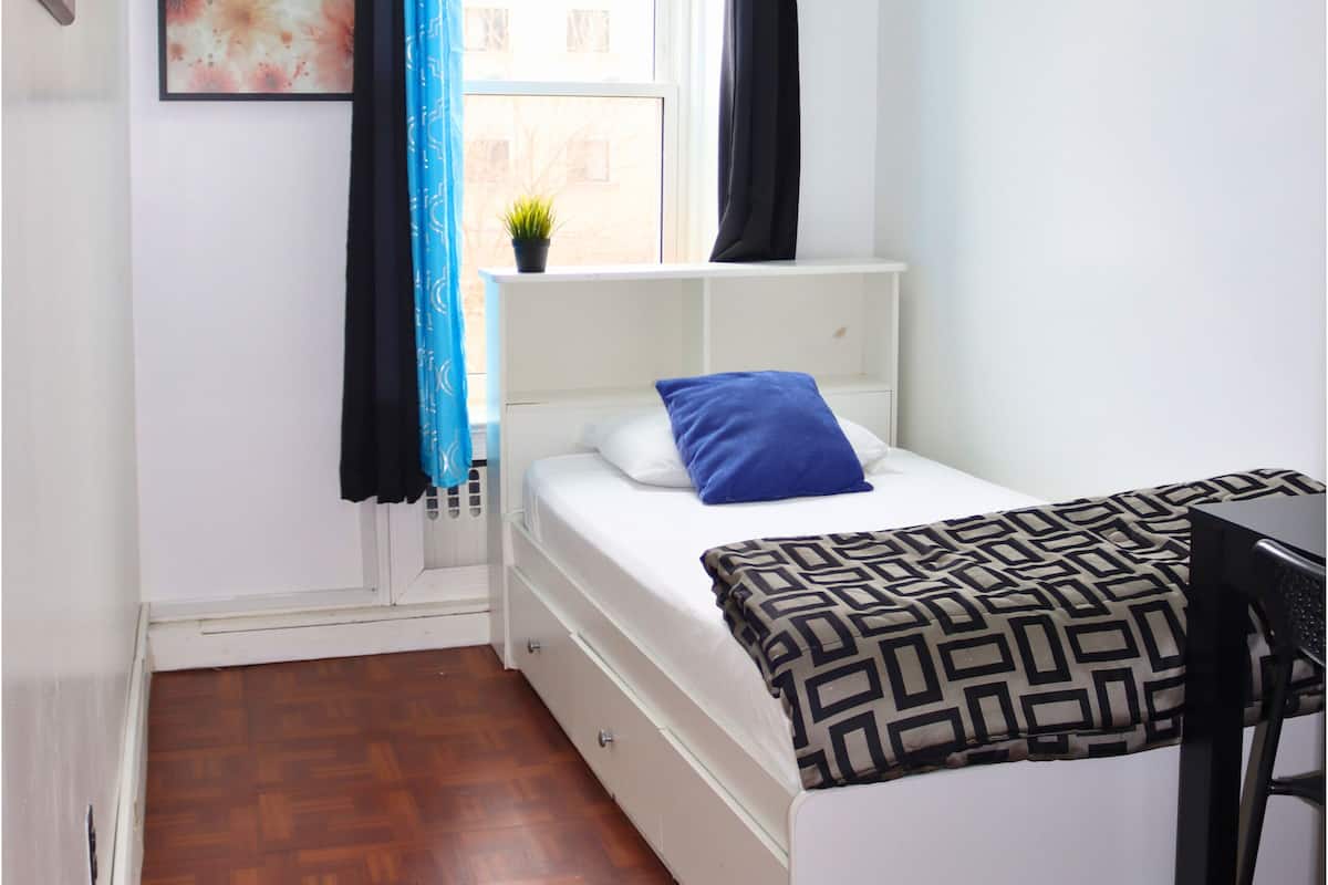 A small, neatly arranged bedroom with a bed, a desk, and a window with curtains.
