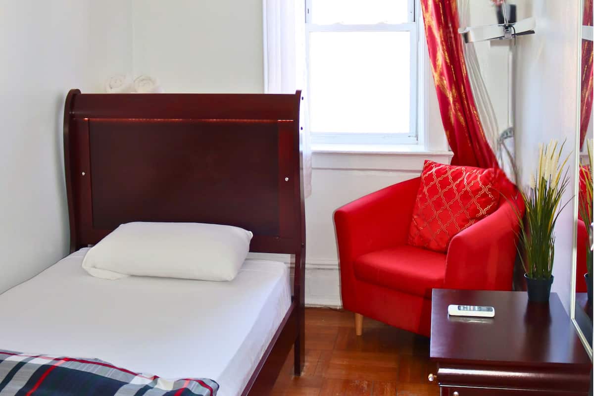 A bedroom with a bed, a red chair, a small desk, and a window with curtains.