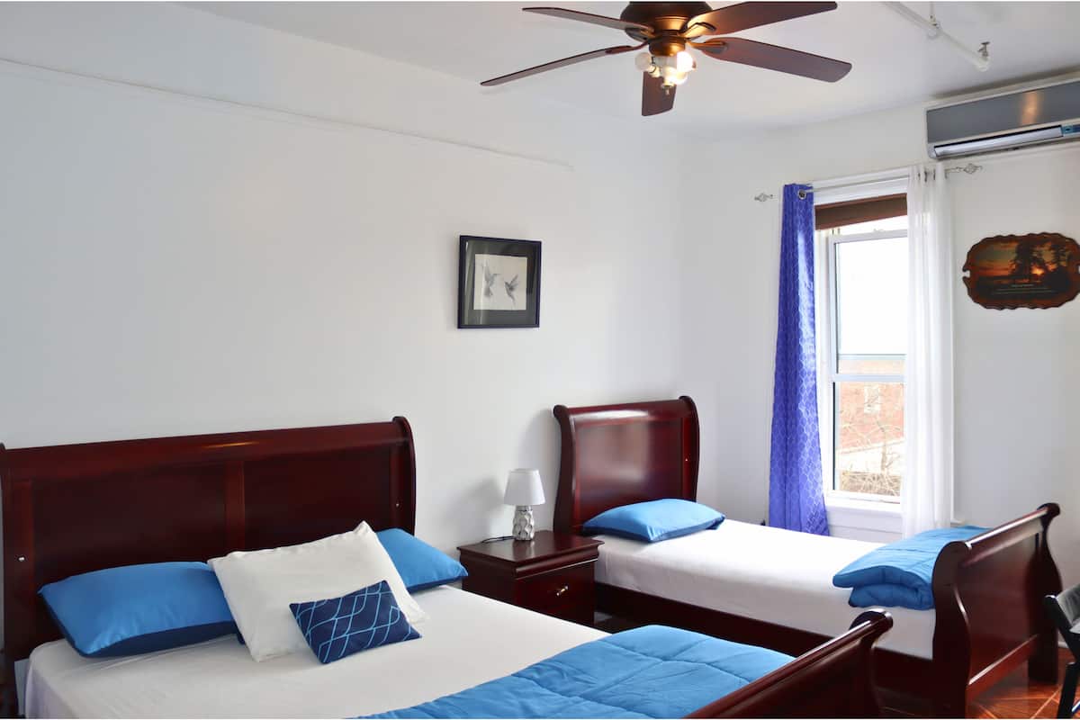 A hotel room with two single beds, a ceiling fan, a window with curtains, and a wall-mounted plaque.