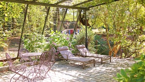 Une terrasse couverte, agrémentée d’une table et de chaises, entourée d’une végétation luxuriante et d’un jardin.