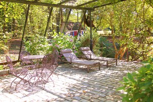 Un patio cubierto con una mesa y sillas, rodeado de exuberante vegetación y un jardín.