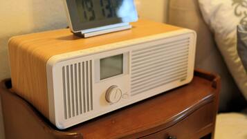 A wooden bedside table with a white radio and a digital clock displaying 7:13.