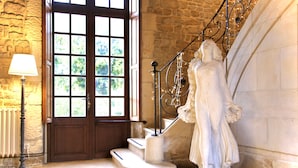 Une statue d’une femme se tenant sur un escalier, avec un mur en pierre et une porte en bois en arrière-plan.