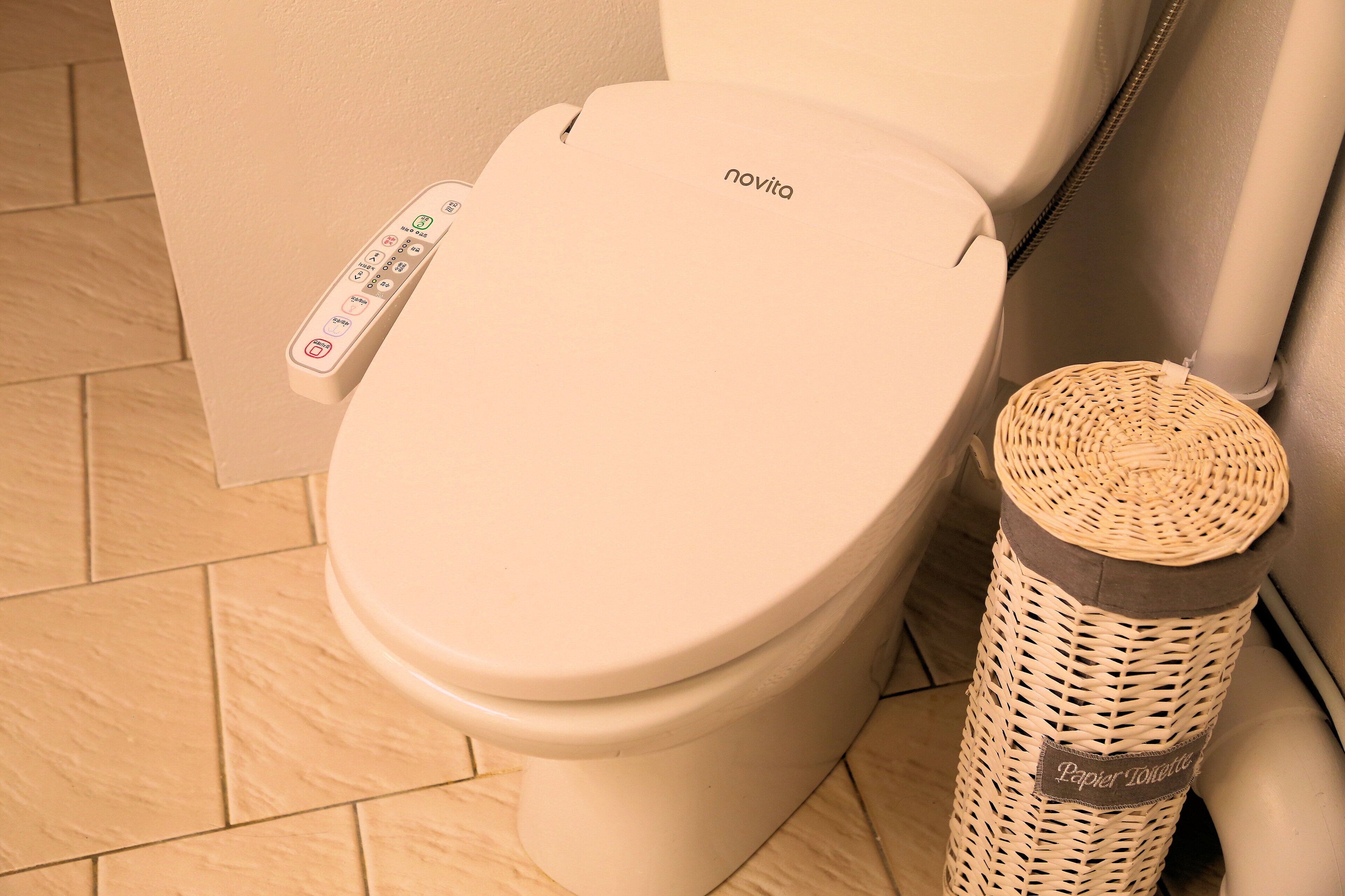 A toilet with a control panel and a wicker trash bin labeled "Papier Tonique".