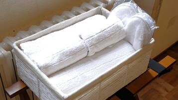 A white, rectangular, insulated storage box with a handle, containing folded white towels and a plastic bag, placed on a wooden floor next to a radiator.