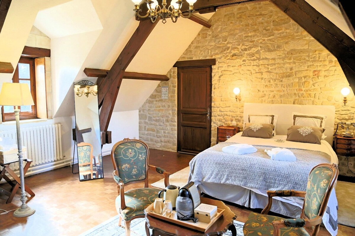 Un dormitorio acogedor con pared de piedra, puerta de madera, cama con almohadas, mesita de noche y una silla.