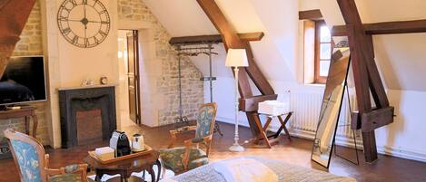A cozy room with a bed, chairs, a fireplace, a clock, and a painting on the wall.