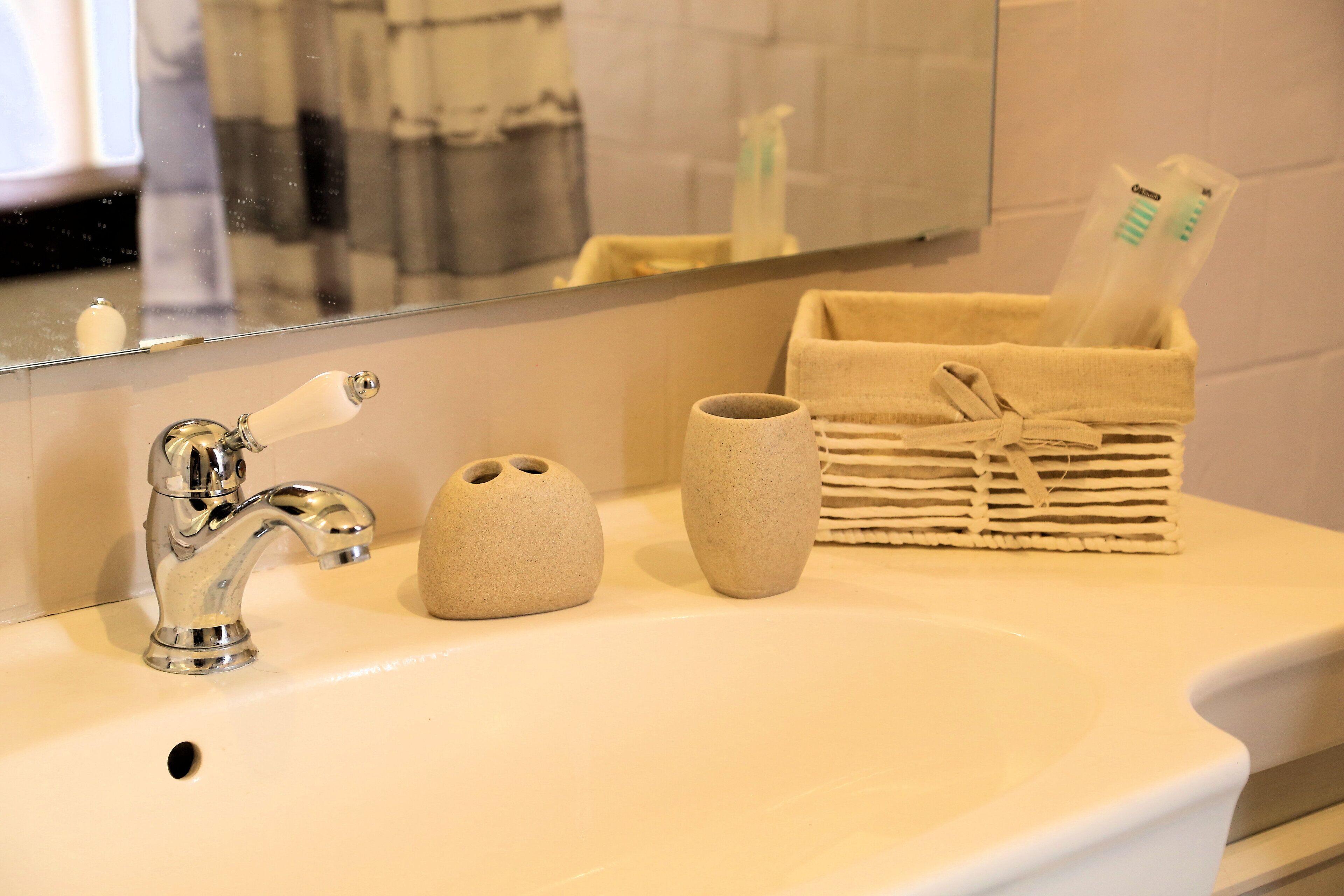 A bathroom sink with a chrome faucet, two ceramic vases, and a basket containing toiletries.