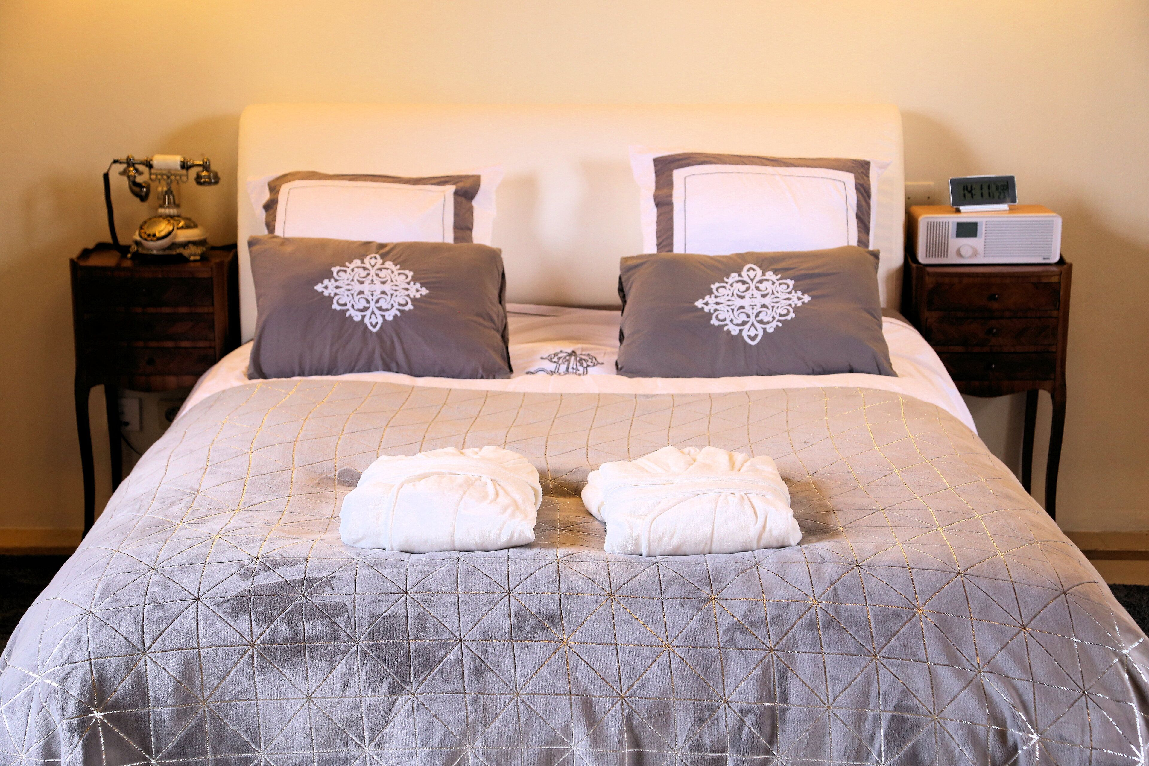 A neatly made bed with a geometric patterned bedspread, two decorative pillows, and two folded towels on the bed.