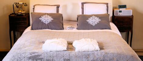 A neatly made bed with a geometric patterned bedspread, two decorative pillows, and two folded towels on the bed.