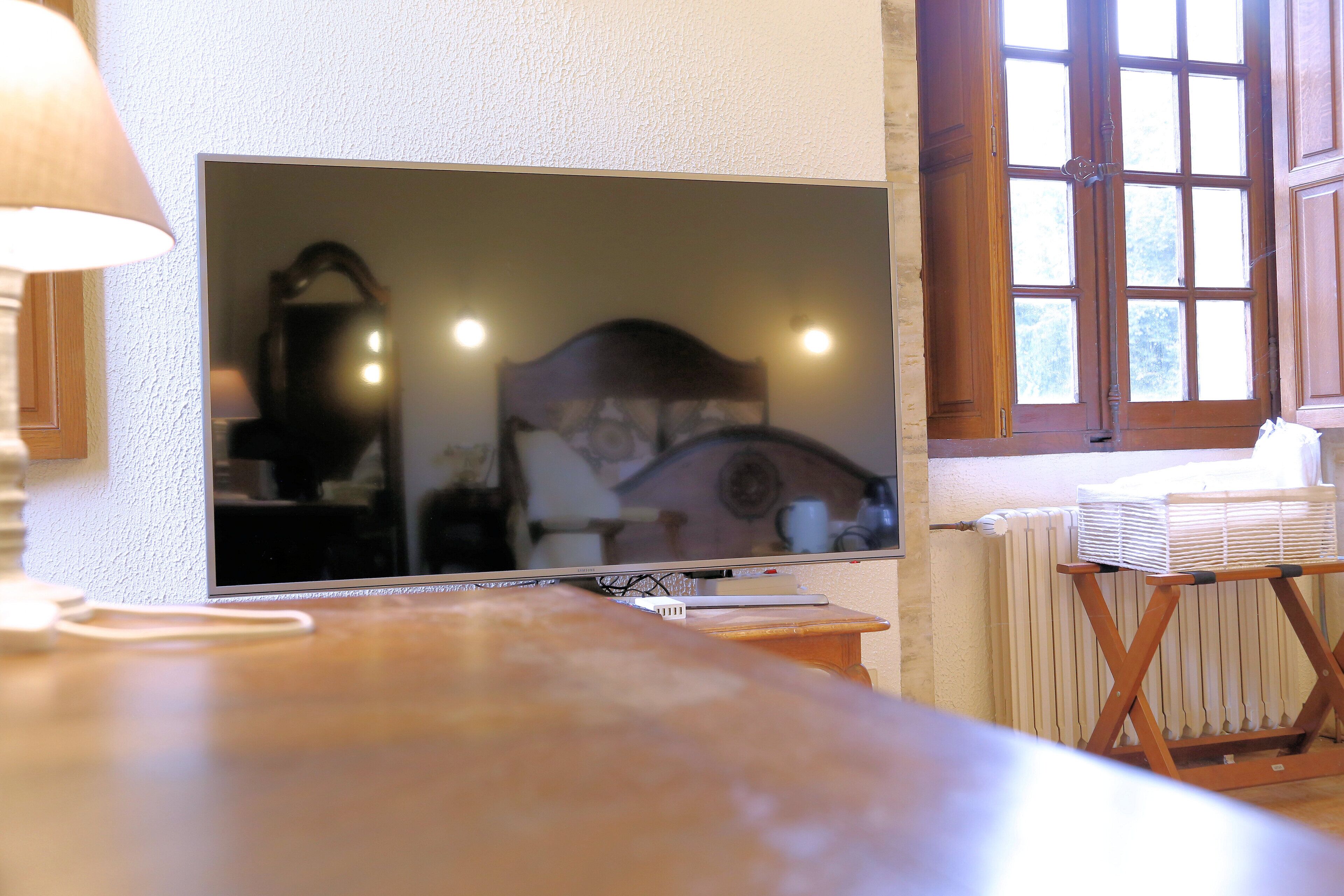 Een kamer met een televisie, een houten tafel, een radiator en een raam met gordijnen.