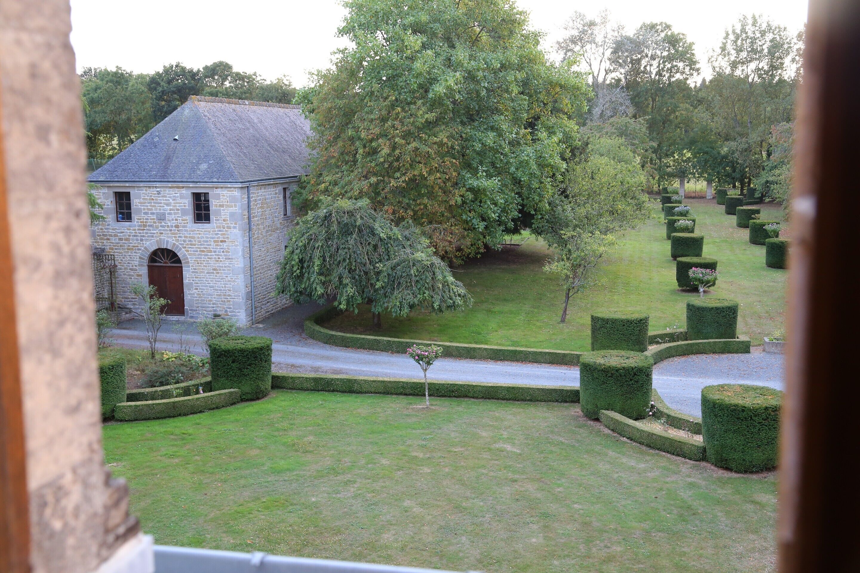 A stone building with a small garden, a tree, and neatly trimmed hedges.