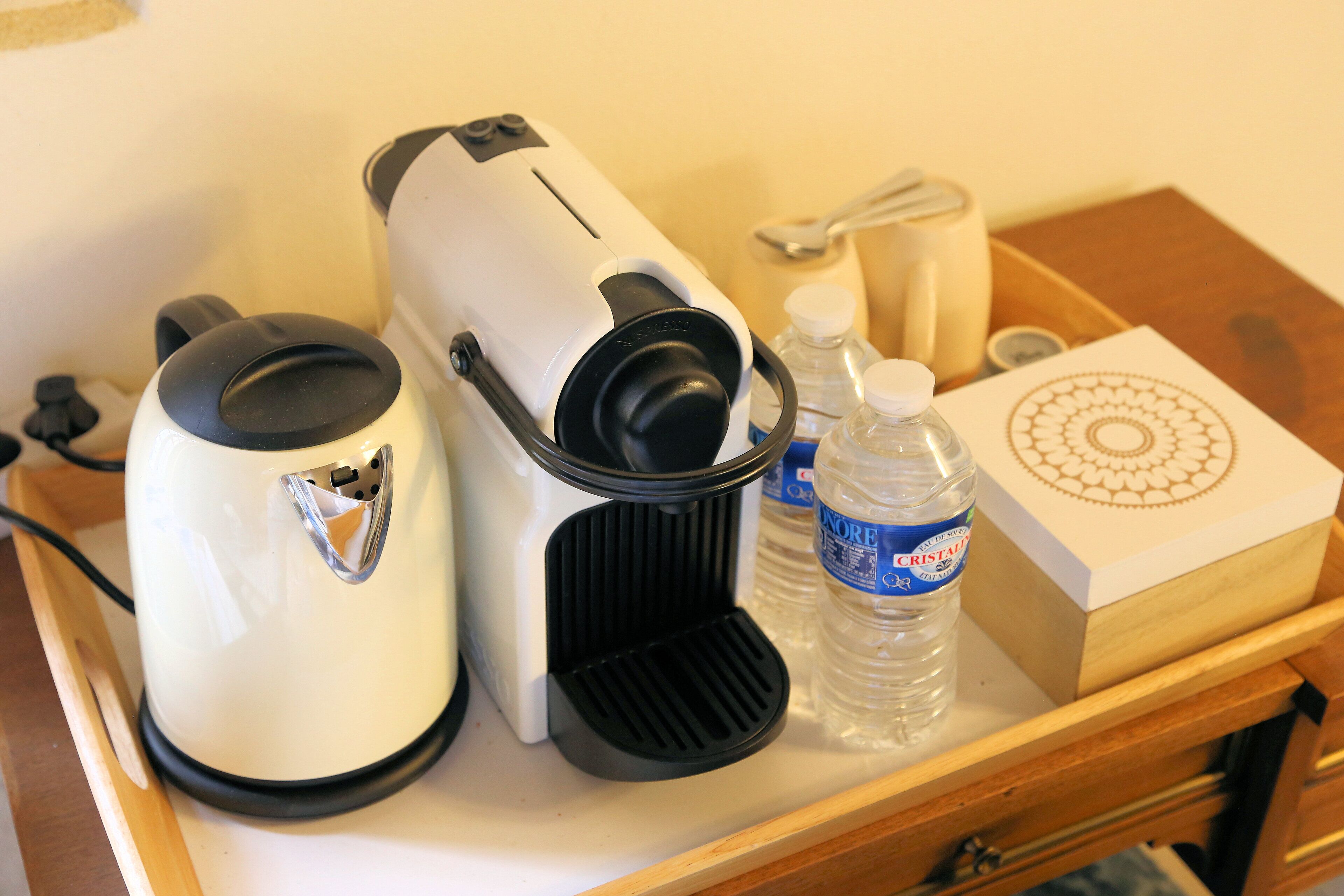 A coffee maker, a water bottle, a spoon, and a decorative box on a wooden tray.