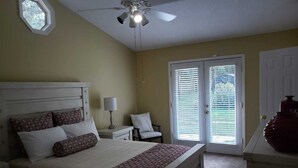 Quarto com cama, mesas de cabeceira, abajur, ventilador de teto e porta com persianas.