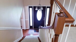 Uma escadaria com corrimãos de madeira e um candelabro, levando a uma porta escura com um aparelho de iluminação acima.