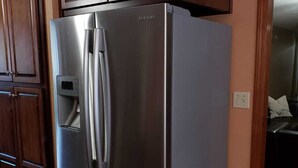 Uma geladeira Samsung de aço inoxidável em uma cozinha com armários de madeira e piso de azulejos.