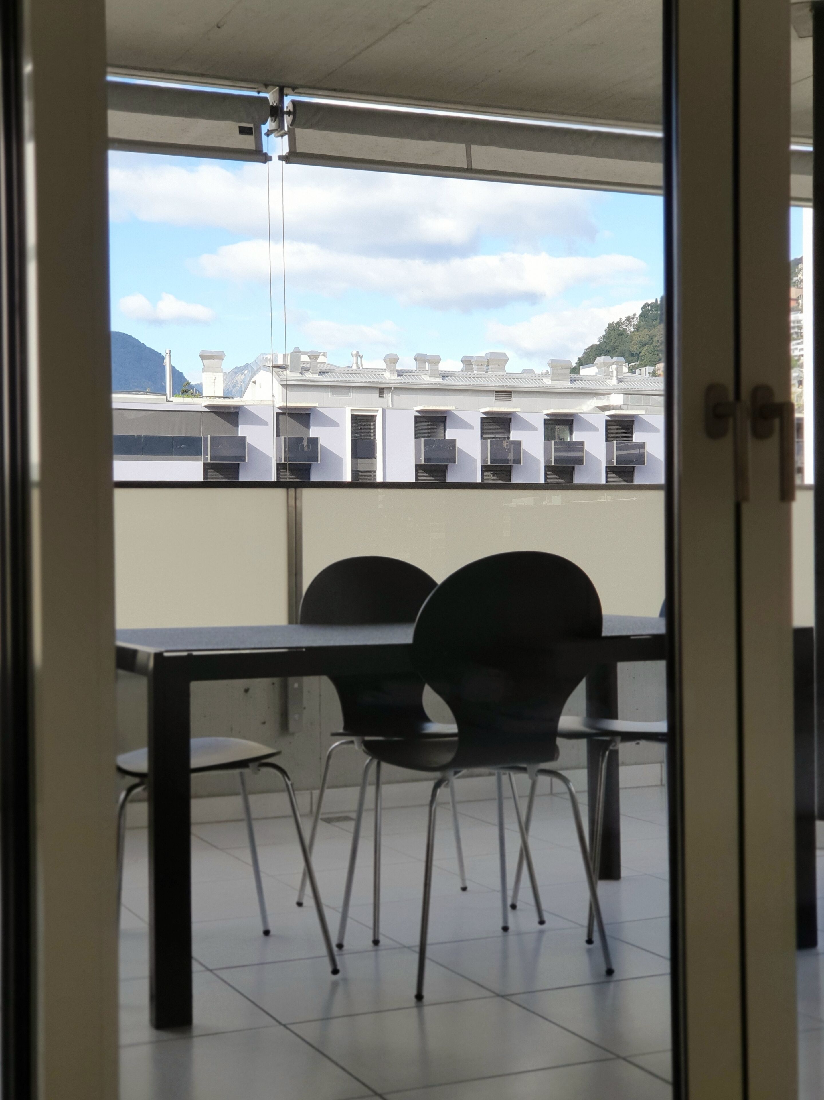 Une vue depuis un balcon, avec une table et des chaises, donnant sur une rangée d’immeubles équipés de climatiseurs.