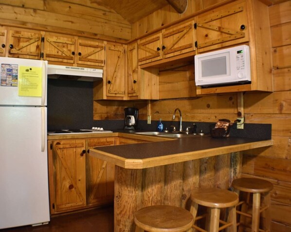 A wooden cabin-style kitchen with a refrigerator, microwave, coffee maker, sink, and wooden stools.