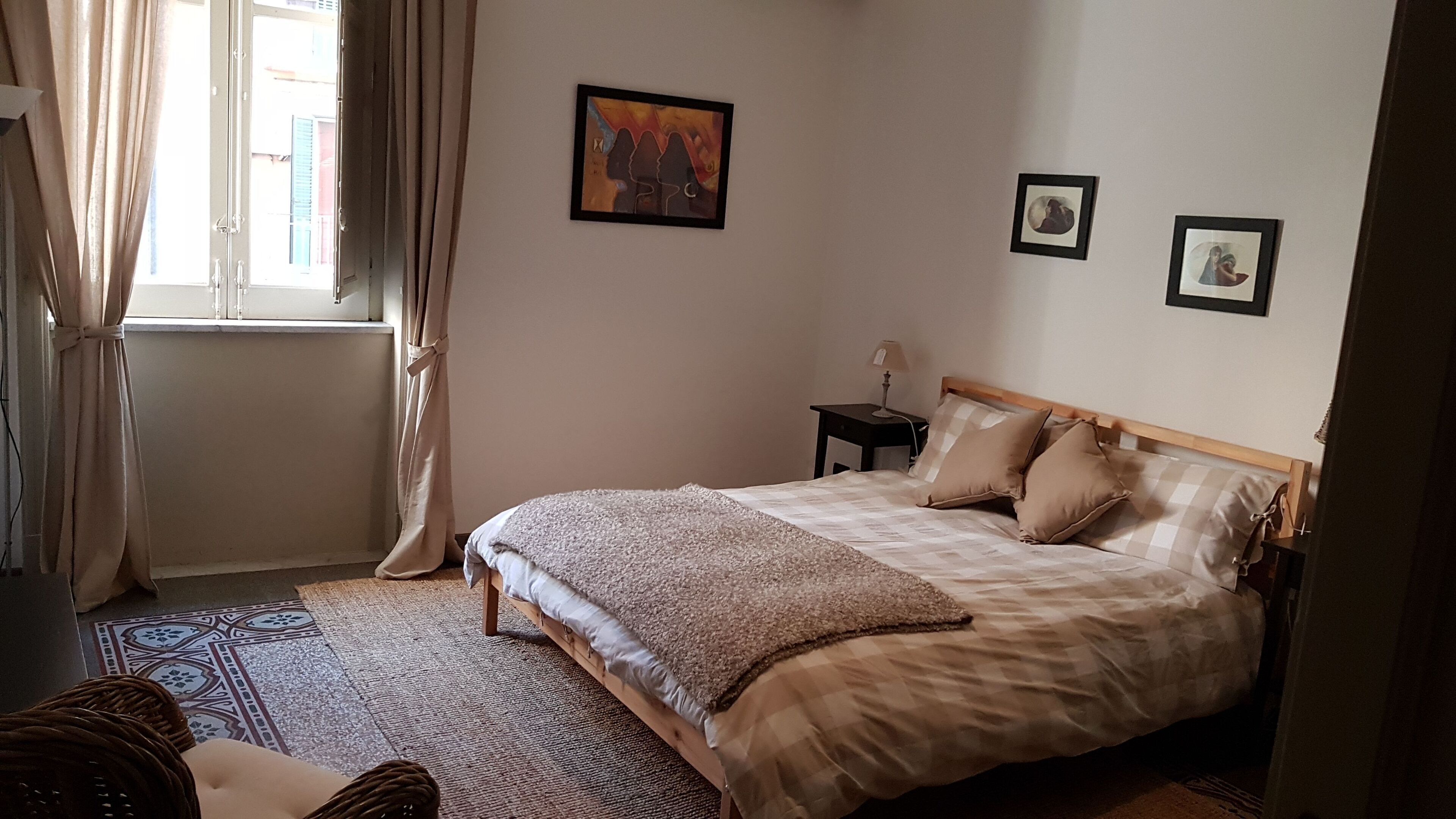 Ein Schlafzimmer mit einem Bett, einem Nachttisch, einer Lampe und einem Fenster mit Vorhängen.