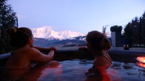 Two individuals in a hot tub with a mountain view in the background. - Vue Mont-Blanc, unique, cosy and natural (CORDON)