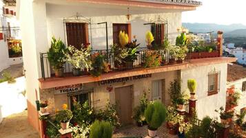 Un bâtiment doté d’un balcon orné de plantes et de fleurs en pot, une enseigne indiquant « CARNICERIA TOBALO », et une vue sur les environs.