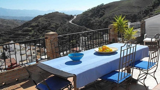 Terraço com uma mesa posta para dois, com vista para uma paisagem montanhosa.
