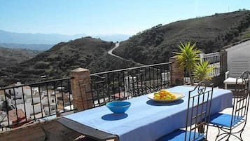 Une terrasse avec une table dressée pour deux personnes, offrant une vue sur un paysage montagneux.
