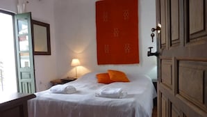 Uma cama bem arrumada com lençóis brancos, um adorno pendurado vermelho e uma porta de madeira.