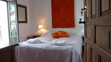 Un lit bien fait, avec du linge de lit blanc, une décoration murale rouge et une porte en bois.