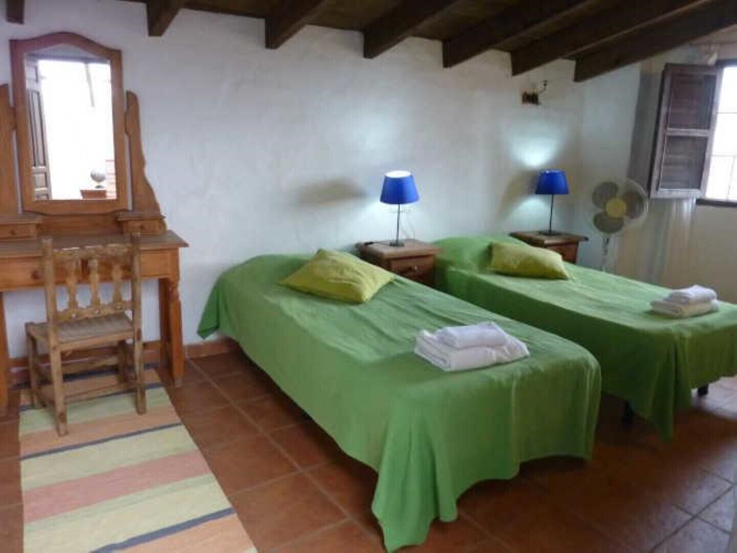 Una habitación con dos camas individuales, una silla de madera, un escritorio y un espejo.