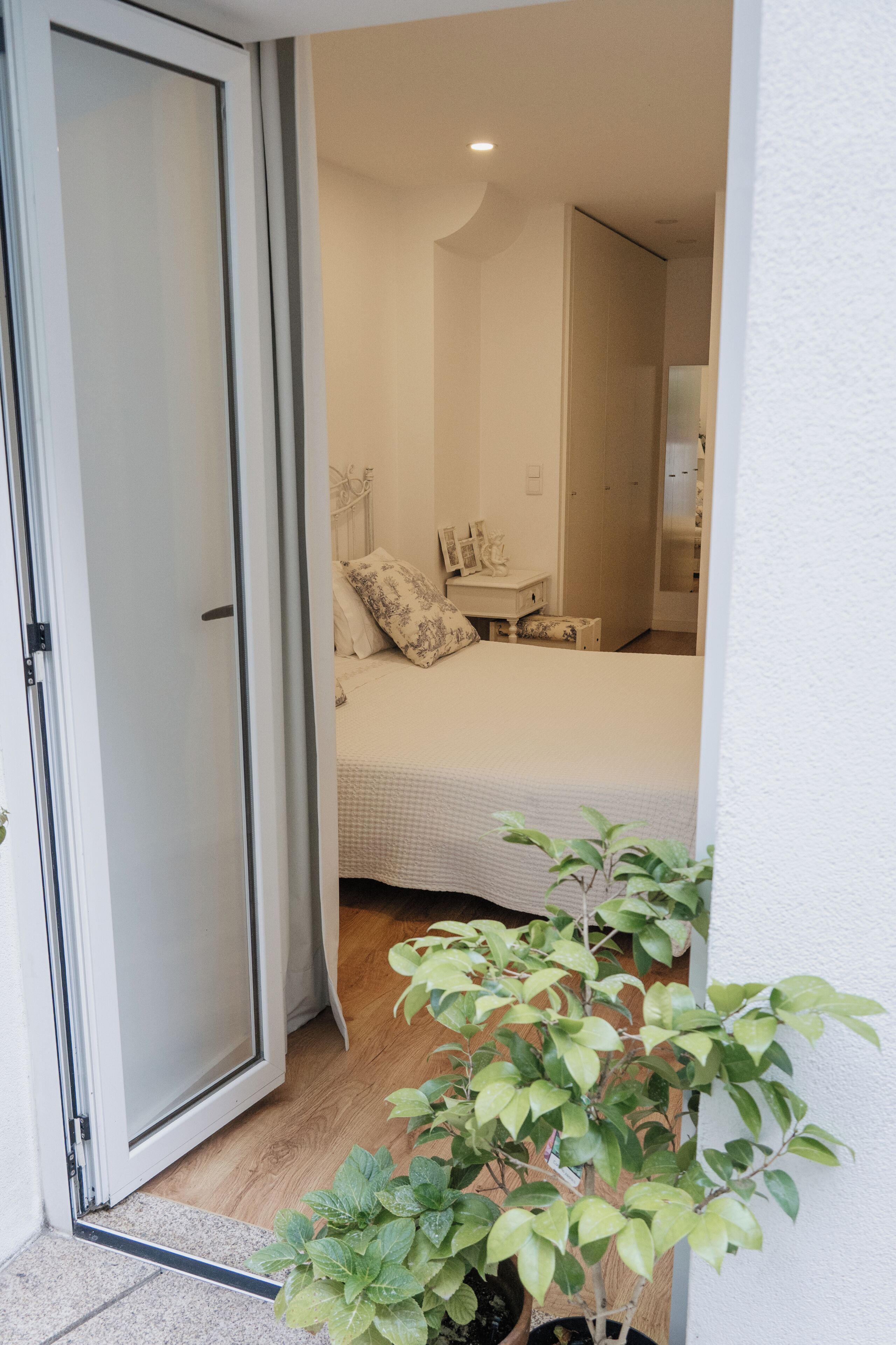 A bedroom with a bed, bedside table, and a potted plant.