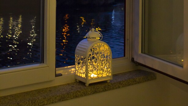 A view from a window with a decorative lantern, a bridge, and city lights reflecting on the water. - Red House by the River (Porto)